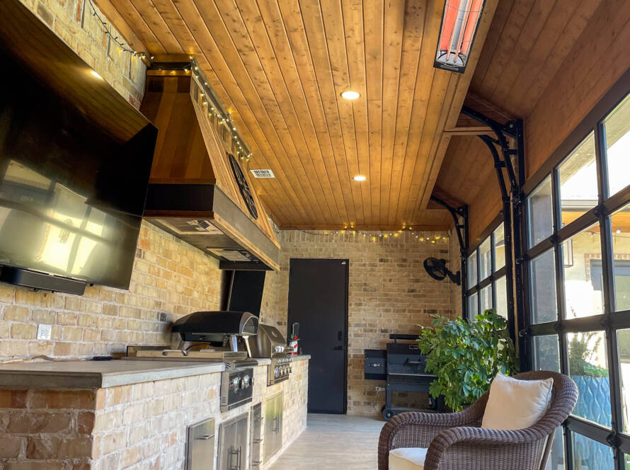 Enclosed outdoor kitchen with stone counters and built-in grill with heaters in Lubbock, TX backyard